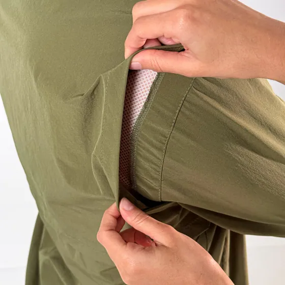 Mão abrindo a aba lateral da camisa verde, revelando a tela de ventilação.